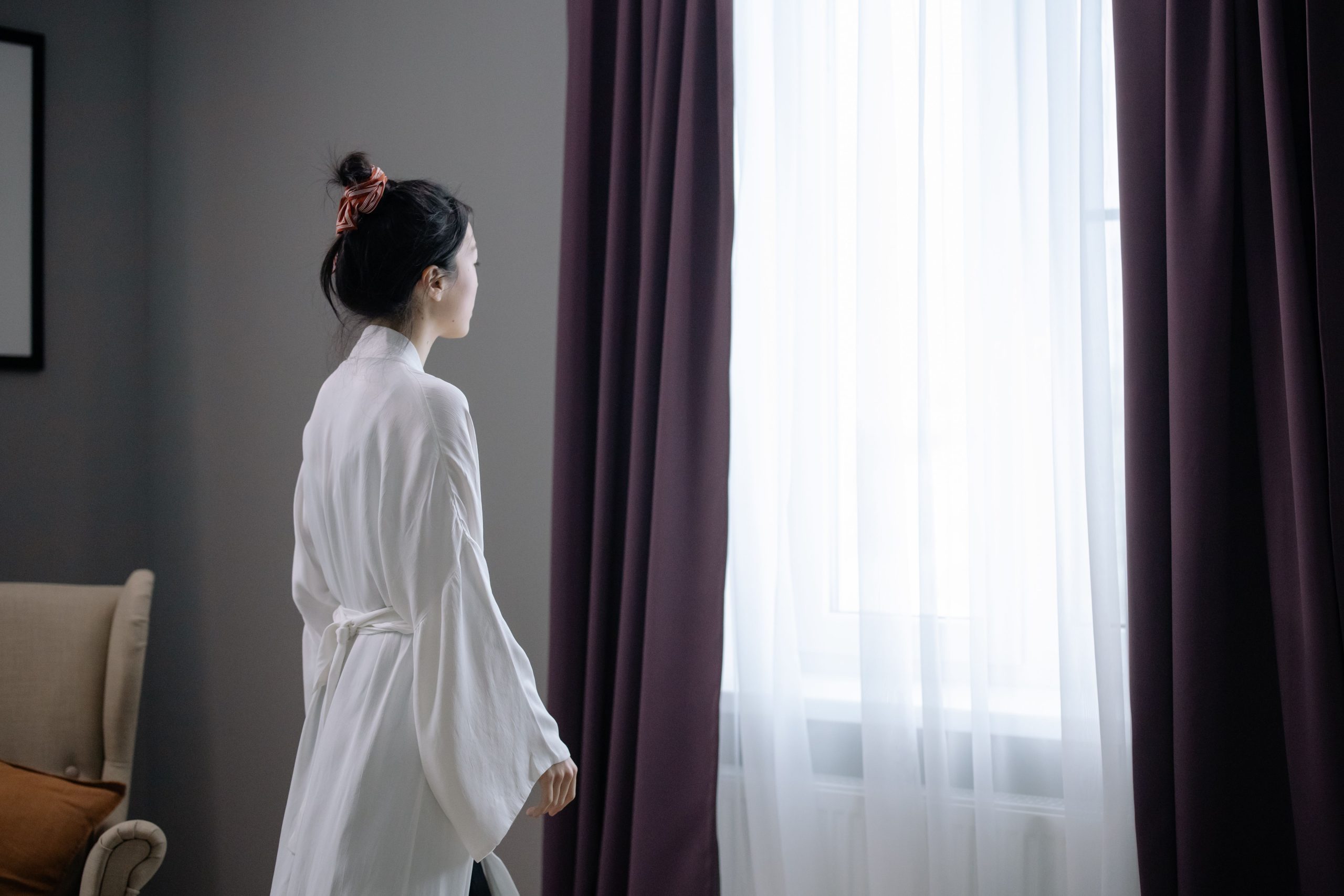 Femme en robe blanche devant une fenêtre voilée
